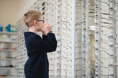 Gözlük takan bir çocuk, optik mağazada çerçeve seçiyor, mükemmel görüş düzeltmesine hazırlanıyor.