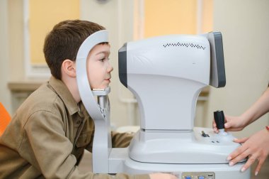 Görme yetisini modern oftalmoloji kliniğinde otomatik fraktör kullanan göz doktoru bir çocuk, sağlık konsepti...