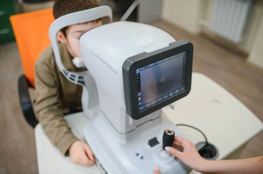 Oftalmolog, tıbbi klinikte genç bir çocuk üzerinde görüş kontrolü yapmak için modern bir otorefraktör kullanır.