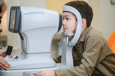 Çocuk hasta, modern klinikte göz doktorunun muayenesi sırasında görme testi için otomatik fraktör kullanıyor.