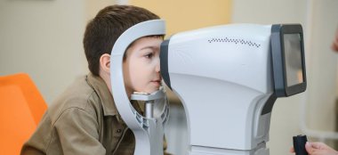 Bir klinikte göz muayenesi için modern oto-fraktör kullanan çocuk, görsel keskinliği ve göz sağlığını kontrol ediyor