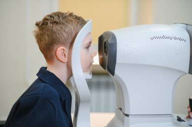 Bir klinikte yapılan göz muayenesi sırasında modern bir otomatik fraktör kullanan bir çocuk.