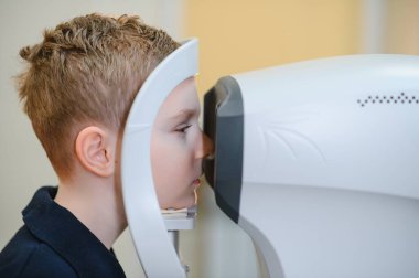 Çocuk hasta, göz muayenesi için modern bir oto-fraktör kullanarak bir göz hekimliği kliniğinde sağlık uzmanlarından özel tedavi görüyor.