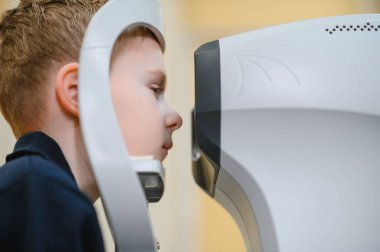 Genç bir çocuk, görüş kliniğinde modern bir oto-fraktör kullanan bir göz doktoru tarafından kontrol ediliyor.