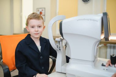 Bir göz hekimliği kliniğinde otomatik fraktör teçhizatı kullanan genç bir çocuk.