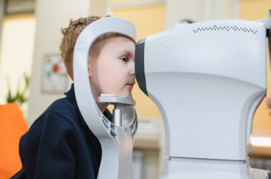 Göz muayenesi sırasında bir göz sağlığı kliniğinde modern bir otorefraktörle meşgul olan çocuk hasta, görme sağlığına odaklanıyor.