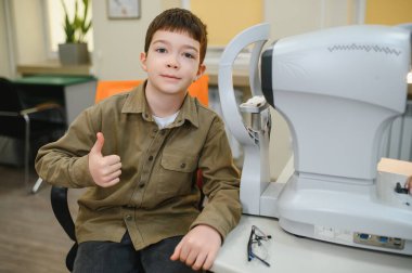 Göz muayenesi sırasında bir göz hekiminde modern ekipmanlarla baş parmak kaldıran genç çocuk olumlu geri bildirim gösteriyor.