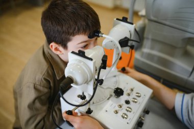 Göz hekimi, göz hekimliği kliniğindeki modern tıbbi ekipmanlarla çocuğun görme yetisini inceliyor.