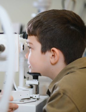 Çocuk hasta, tıbbi bir klinikte modern bir teşhis cihazı kullanarak bir göz doktoru tarafından muayene ediliyor.