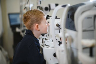 Çocuk görüş kliniğinde modern göz doktoru teçhizatı kullanarak görme testi yaptırıyor.