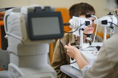 Oftalmolog, tıbbi klinikte uzman göz bakımı sağlayan bir çocuğun vizyonunu kontrol etmek için modern ekipmanlar kullanıyor.