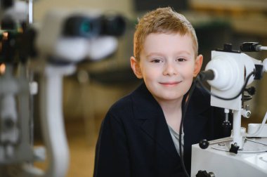 Gülümseyen çocuk tıbbi klinikte modern oftalmolojik ekipman kullanarak vizyon kontrolünden geçiyor.