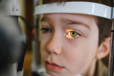 Görme kliniğinde uzman bir tıbbi cihaz kullanan bir göz doktoru tarafından göz muayenesi yapılan bir çocuğun yakın çekimi.