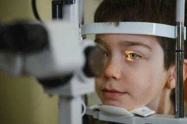Çocuk, modern bir göz kliniğinde kesik lamba kullanarak göz doktoru tarafından göz muayenesi yaptırıyor.