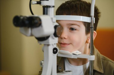 Genç bir çocuğun modern bir göz kliniğinde fosfor kullanan bir göz doktoru tarafından gözleri kontrol ediliyor.