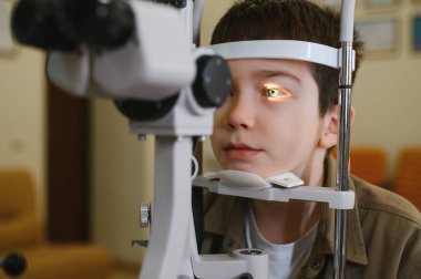 Genç bir çocuk, tıbbi klinikteki bir göz doktoru tarafından modern bir yarık lambasıyla biyomikroskopla inceleniyor.
