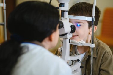 Vizyon kliniğinde çalışan bir kadın göz doktoru tarafından desteklenen kesik lamba biyomikroskobu kullanılarak göz muayenesinden geçen bir çocuk.