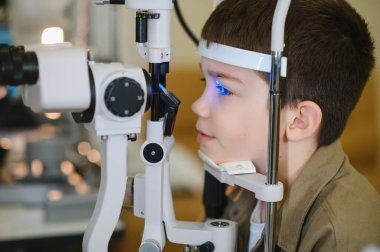 Çocuk, modern bir klinikte kesik lamba kullanarak bir göz doktoru tarafından kontrol ediliyor.
