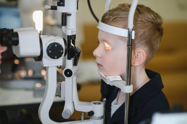 Genç bir çocuk, modern bir göz kliniğindeki bir göz doktoru tarafından kesik lamba ile biyomikroskopa tabi tutuluyor.