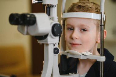 Modern bir oftalmoloji kliniğinde phoropter kullanılarak göz muayenesine tabi tutulan çocuk hasta, doğru teşhis ve tedaviyi garanti altına alıyor.