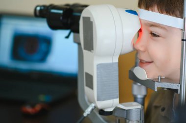 Bir klinikte otomatik fraktör kullanan bir göz doktoru tarafından gözleri kontrol edilen gülümseyen bir çocuk.