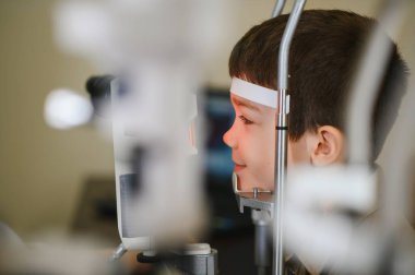 Görme yeteneğini göz hekimliği kliniğindeki tıbbi ekipmanlarla kontrol ettiren genç bir çocuk sağlıklı bir görüş sağlıyor.