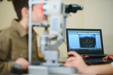 Oftalmolog, genç bir çocuğun vizyonunu incelemek için özel ekipman kullanır ve teşhis sonuçlarını bir dizüstü bilgisayarda gösterir.