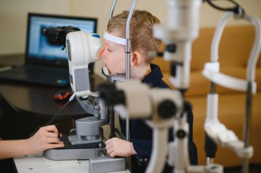 Oftalmolog, bir görüş merkezinde modern bir oto-fraktör kullanan genç bir çocuğun görme yeteneğini inceliyor.
