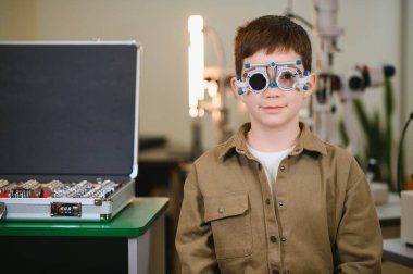 Deneme çerçevesi takan genç bir çocuk göz doktorunun kliniğinde görme ve göz sağlığına odaklanmış bir göz muayenesinden geçiyor.