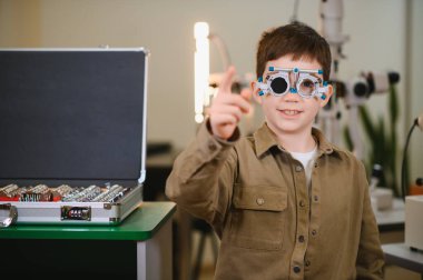 Göz muayenesi sırasında göz teması kuran gülümseyen bir çocuk göz muayenesinden zevk alıyor.