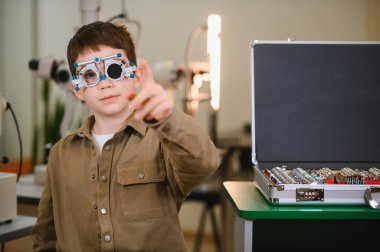 Görme testi sırasında parmağıyla işaret eden genç hasta göz doktorunun ofisinde deneme çerçevesi takıyor.