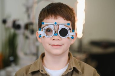 Bir göz doktorunun muayenehanesinde göz muayenesi yapılırken, görme sağlığı ve bakımı üzerine çalışan bir çocuk.