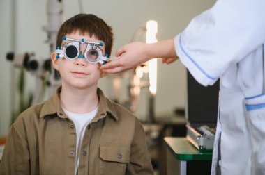 Bir tıp kliniğinde görme testi sırasında genç bir çocuğun yüzüne bir deneme çerçevesi yerleştiren oftalmolojist, doğru bir göz bakımı sağlıyordu.