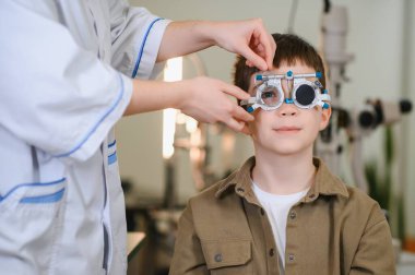 Göz doktoru, gözlük için doğru reçeteyi belirlemek için deneme çerçevesi kullanan bir çocuk üzerinde göz muayenesi yapıyor.