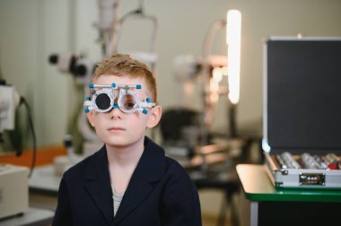 Bir göz sağlığı kliniğinde göz muayenesi yapılırken çocuk bir deneme çerçevesi takıyor, görme ve göz sağlığını değerlendiriyor.