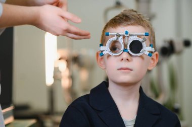 Genç bir çocuk modern bir klinikte göz muayenesi sırasında bir phoropterle görme testinden geçiyor.