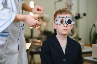 Doktor göz doktoru, göz hekimliği kliniğinde muayene sırasında küçük bir çocuğun görme yetisini test ediyor.