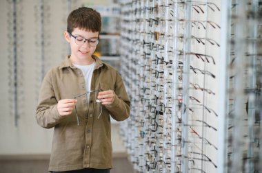Bir optik mağazada yeni gözlük deneyen genç çocuk, gelişmiş görme ve şık çerçevelerle gelişmiş göz sağlığına hazırlanıyor.