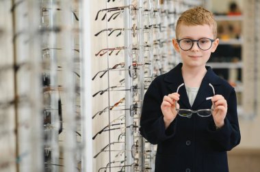 Çocuk optik mağazasında yeni gözlük deniyor, mükemmel görüş düzeltmesi için çeşitli çerçeveleri keşfediyor.