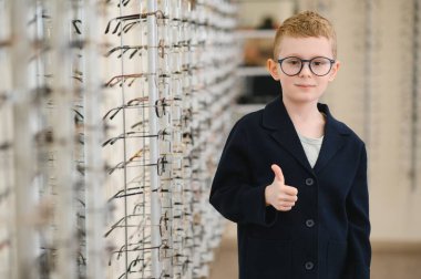 Gözlük dükkanında gözlük seçtikten sonra başparmağını kaldıran çocuk, yeni gözlüklerden memnun.