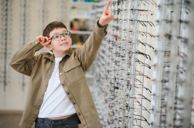 Gözlük deneyen çocuk, optik mağazada çerçeve seçen çocuk, çocuklar için görüş düzeltmesi, göz hekimi kliniği