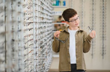 Gözlükleri optik mağazada karşılaştıran bir çocuk görme düzeltmesi hakkında bilgilendirilmiş bir karar veriyor.