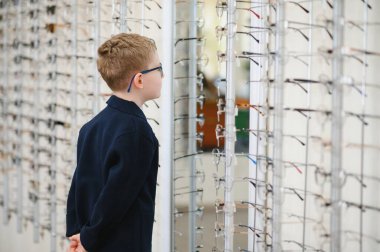 Bir optik mağazada çeşitli gözlük deneyen çocuk, gelişmiş görme ve daha iyi görme için şık seçenekler keşfetmeye hazırlanıyor.