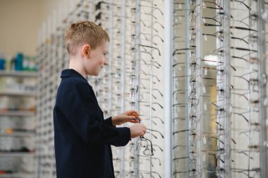 Gülümseyen çocuk optik bir dükkanda gözlük seçerek, görüş bakımı için mükemmel çerçeveleri seçmenin tadını çıkarıyor.