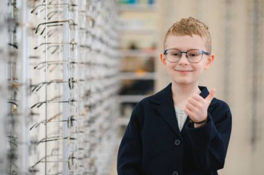 Yeni gözlük takan gülümseyen çocuk optik mağazasında baş parmak işareti gösteriyor, mükemmel görüşünden memnun.