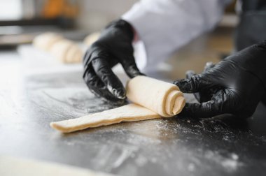 Siyah eldivenli fırıncı lezzetli kruvasanlar için mükemmel bir spiral oluşturuyor. Profesyonel bir fırın mutfağında uzmanlık gösteriyor.