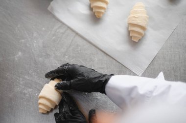 Siyah eldiven giyen fırıncı, kruvasan hamurunu diğer kruvasanların yanına, bir fırın kağıdına koyar.