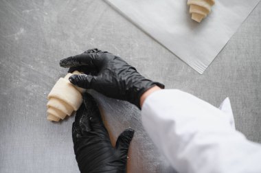 Fırıncı fırınının mutfağında, kruvasan hamurunu ustalıkla hazırlayan siyah eldivenli fırıncı fırın fırınına odaklandı.