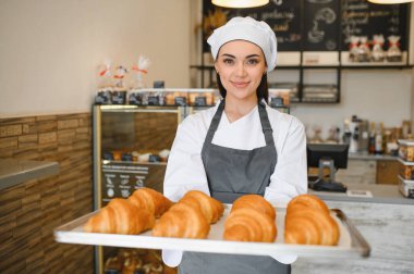 Baker gururla fırınında bir tepsi altın sarısı kruvasan sunar. Pişirme becerilerinin leziz sonuçlarını gözler önüne serer.