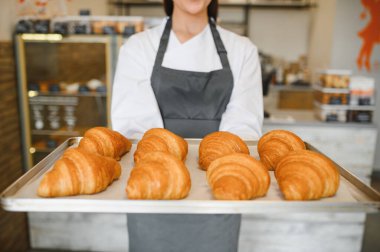 Baker bir tepsi altın kahverengi kruvasan sunuyor, fırının taze ve lezzetli hamur işlerini gösteriyor.